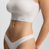 Person wearing a white sports bra and underwear set on a light gray background