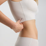 Person wearing a white sports bra and underwear set on a light gray background