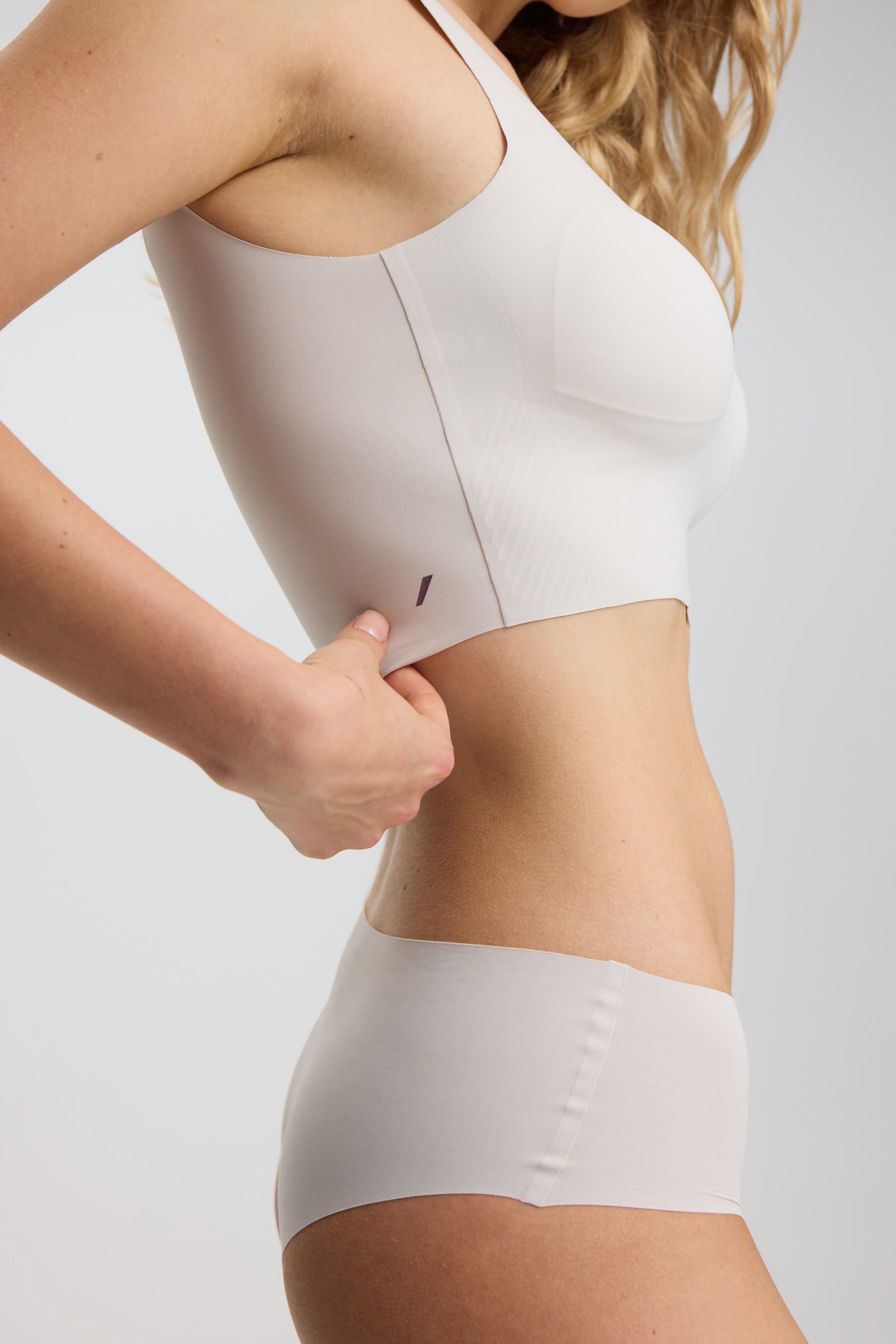 Person wearing a white sports bra and underwear set on a light gray background